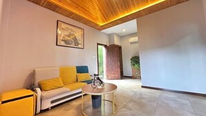 A modern living room with a wooden ceiling, a sofa with yellow cushions, a round coffee table, and a framed picture on the wall. - China Magnetic Mountain Springs Park (Yantai)