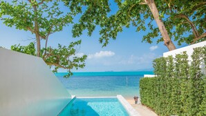 An infinity pool with a view of the ocean, two wooden chairs with cushions, and a white wall. - White Whale Beachfront Pool Villa (Koh Samui)