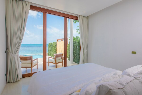 A bedroom with a large bed, a view of the ocean, and a balcony with chairs. - White Whale Beachfront Pool Villa (Koh Samui)
