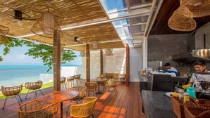 A restaurant with outdoor seating overlooking the sea, featuring wicker chairs and tables, a bar area, and a view of the ocean. - White Whale Beachfront Pool Villa (Koh Samui)