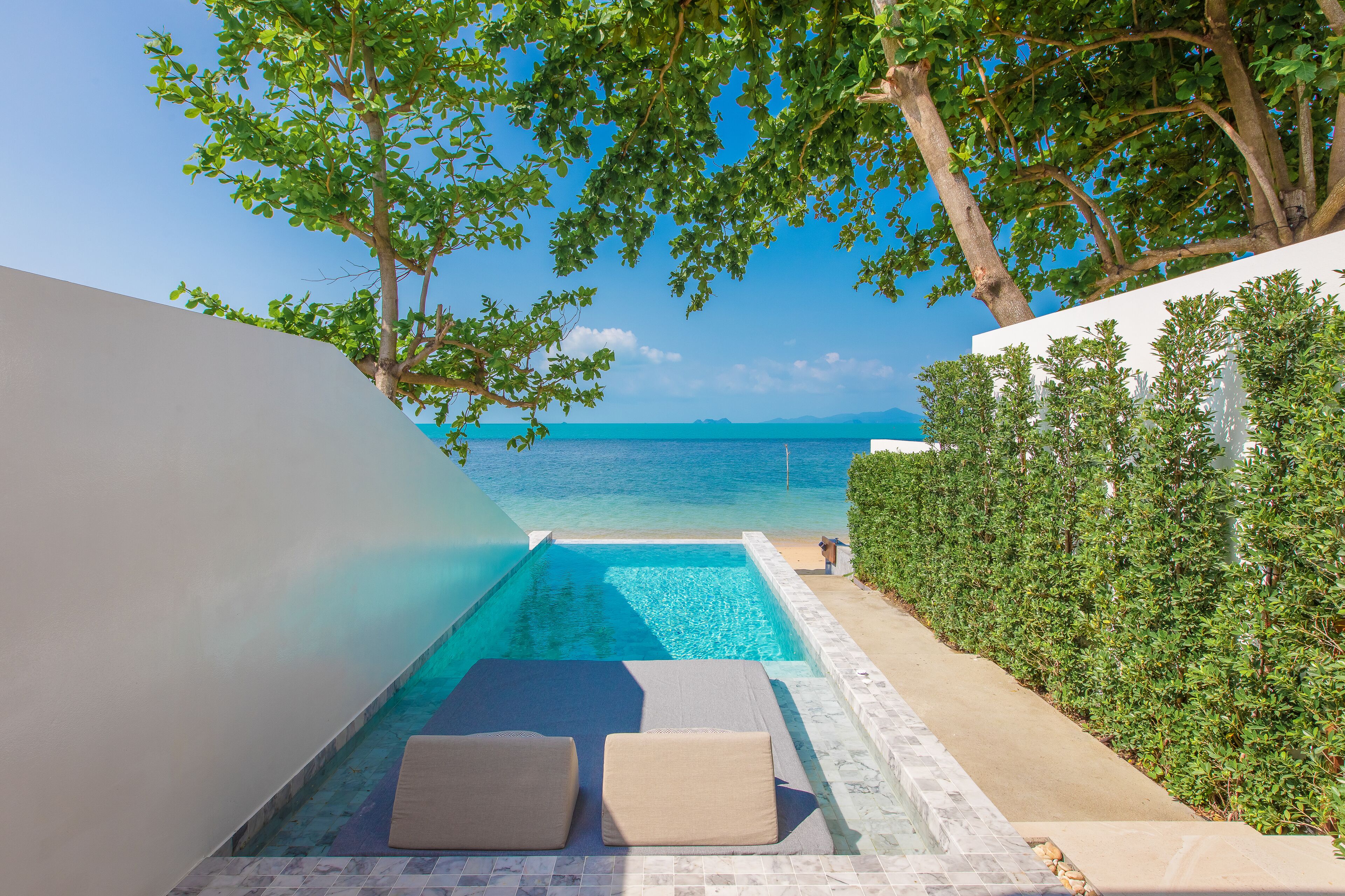 A private pool area with lounge chairs, a clear view of the sea, and a hedge along the side.