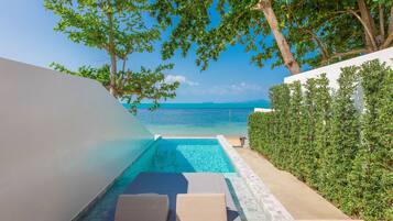 A private pool area with lounge chairs, a clear view of the sea, and a hedge along the side.