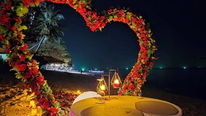 A heart-shaped floral arch with candles and a table set for two on a beach at night. - White Whale Beachfront Pool Villa (Koh Samui)