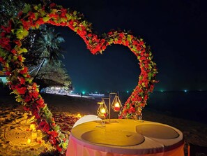 A heart-shaped floral arch with candles and a table set for two on a beach at night. - White Whale Beachfront Pool Villa (Koh Samui)