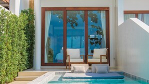 A modern pool area with a clear blue pool, wooden deck, and a seating area with two chairs and cushions. - White Whale Beachfront Pool Villa (Koh Samui)