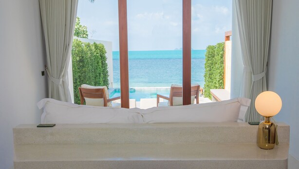 A bedroom with a view of the sea, a bed, a bedside table with a lamp, and a chair. - White Whale Beachfront Pool Villa (Koh Samui)