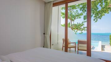 A bedroom with a large bed, a chair, and a view of the ocean through a sliding glass door.