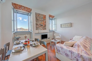 Ein Zimmer mit Esstisch für Zwei, einer Couch, einem Fernseher und einem Kamin.