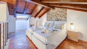 A bedroom with two beds, a stone wall, wooden beams, and a skylight. - Incanto Sul Lago: Arona Lakefront Apartment with A/C, Arona, Italy (Arona)