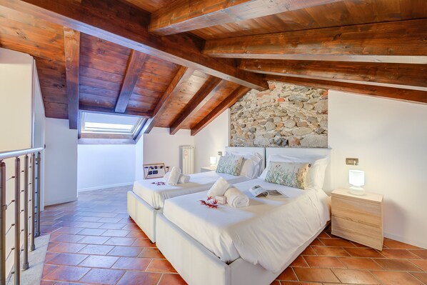 Un dormitorio con dos camas, pared de piedra, vigas de madera y tragaluz.