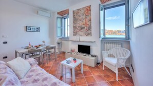 A living room with a sofa, a dining table, a TV, and a fireplace. - Incanto Sul Lago: Arona Lakefront Apartment with A/C, Arona, Italy (Arona)