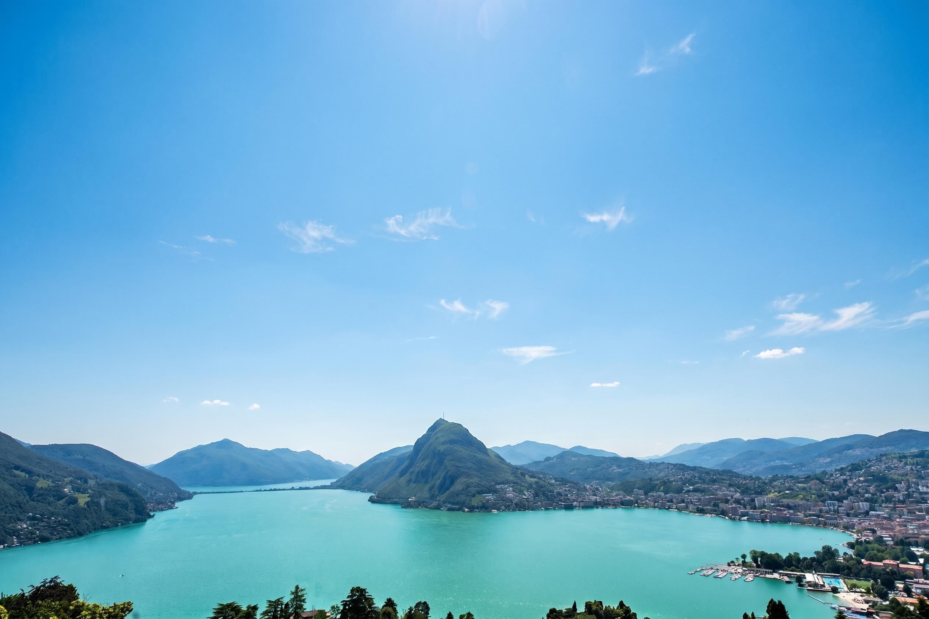 A panoramic view of a lake surrounded by mountains, with a clear sky.