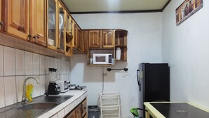 Une cuisine compacte avec des meubles en bois, un four à micro-ondes, un réfrigérateur noir, un évier, un mixeur et une petite table à manger avec des chaises.