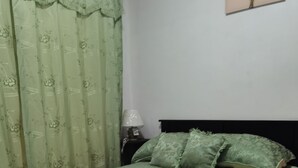 Un lit recouvert d’une couvre-lit à motifs floraux verts, une table de chevet avec une lampe et un mur orné d’un tableau encadré.