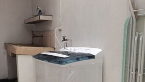 Une petite buanderie comprenant un lave-linge, un petit évier et un étendoir.