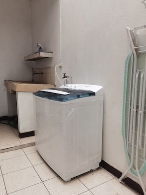 A compact laundry room with a washing machine, a small sink, and a drying rack.