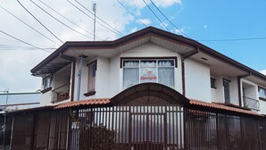 Une maison à deux étages, dotée d’une entrée fermée par un portail, d’un balcon à l’étage supérieur et d’une enseigne au-dessus de l’entrée principale.