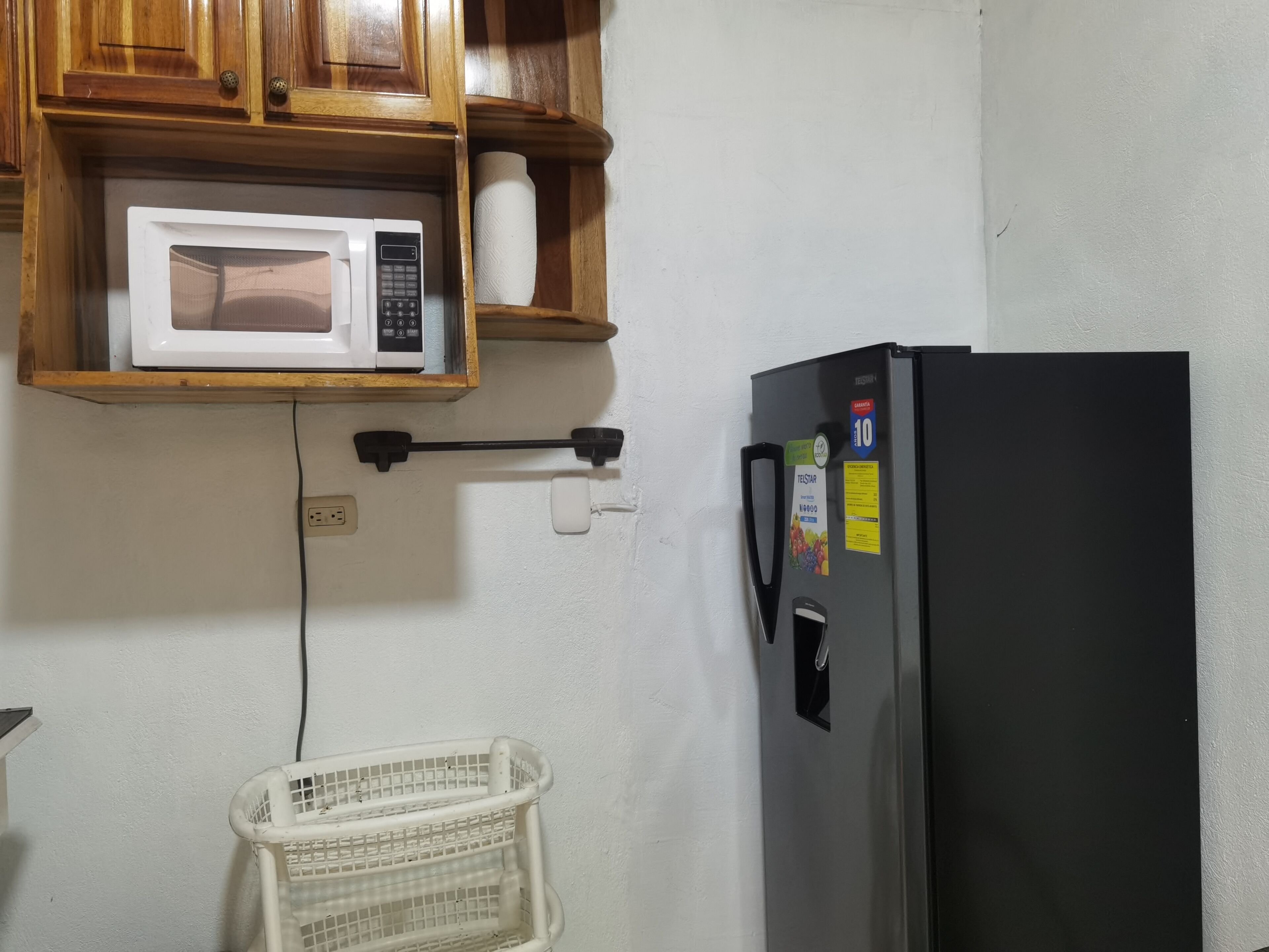 Een keuken met een magnetron op een houten plank, een zwarte koelkast en een witte mand op de vloer.