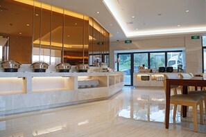 A modern hotel lobby with a reception desk, buffet area, and a dining area with a wooden table and chairs.