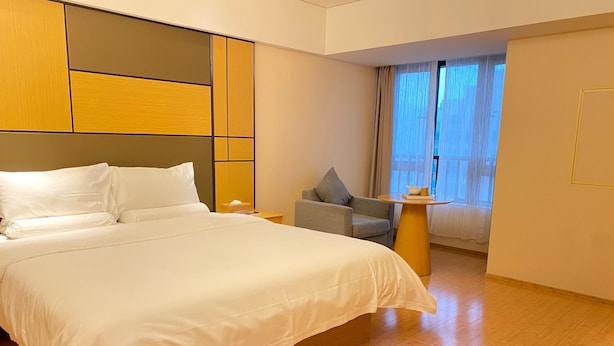 A hotel room with a large bed, a small table, a chair, and a window with curtains. - Ji Hotel Xiamen Sm Plaza Chenggong Avenue (Chuzhou)