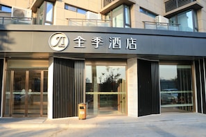 A hotel entrance with a modern facade, large glass doors, and a trash bin outside.
