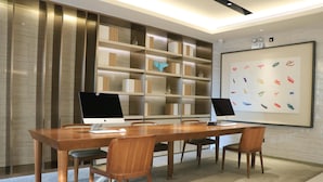 A modern meeting room with a long wooden table, four chairs, two desktop computers, a large bookshelf, and a framed artwork on the wall. - Ji Hotel Xiamen Sm Plaza Chenggong Avenue (Chuzhou)