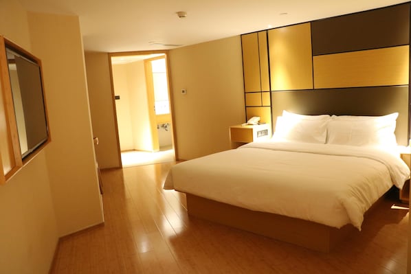 A hotel room with a large bed, a bedside table with a lamp, and a door leading to another room.