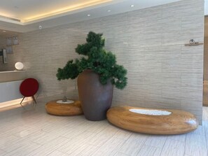 A reception area with a modern design, featuring a large potted plant, wooden seating, and a reception desk. - Ji Hotel Xiamen Sm Plaza Chenggong Avenue (Chuzhou)
