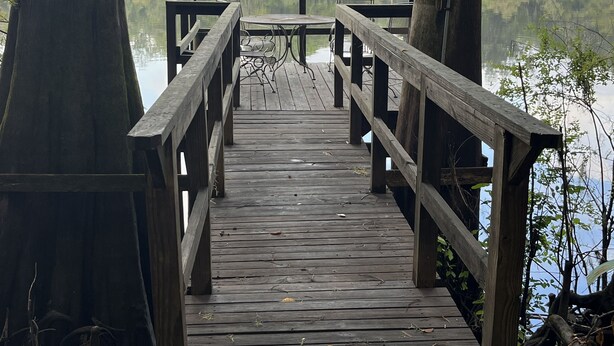 A wooden pier leading to a small table and chairs overlooking a calm body of water, surrounded by trees. - Bell, Fl  3/2 home on Suwannee w/boat ramp (Bell)