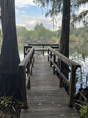 A wooden pier leading to a small table and chairs overlooking a calm body of water, surrounded by trees. - Bell, Fl 3/2 home on Suwannee w/boat ramp (Bell)