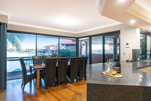 A dining area with a table and chairs, a kitchen counter with a bottle and glass, and large windows with a view of buildings and palm trees.