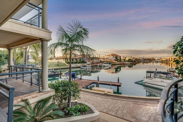 A marina with boats docked, a palm tree, and a building with a balcony overlooking the water.