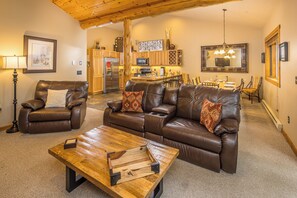 A spacious living area with leather sofas, a wooden coffee table, and a kitchen in the background. - Big Sky Condo! Private Hot Tub & Sauna! Mountain Views! (Big Sky)