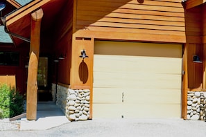 Ein Holzhaus mit einer Garagentür, Steinpfeilern und einer Glocke an der Wand.