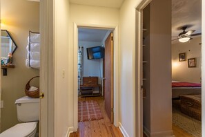 Ein Flur mit Holzboden, einer weißen Toilette, einem an der Wand montierten Fernseher und einem Deckenventilator.