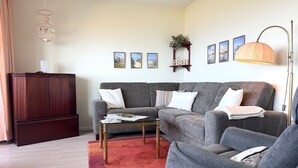 Ein Wohnzimmer mit grauem Sofa, einem Holzkabinett, einem roten Teppich und einer Stehlampe.