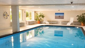 Una piscina interior con agua cristalina, rodeada de sillones de descanso y plantas en macetas.