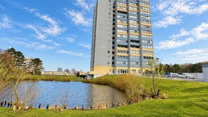 Un edificio residencial de varios pisos con techo plano, un pequeño estanque y un área verde al frente.