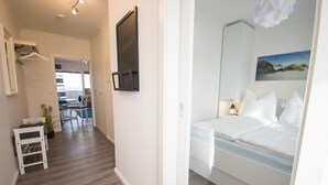 Habitación de hotel con cama, mesita de noche, televisor empotrado en la pared y un cuadro.