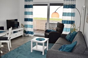Ein modernes Wohnzimmer mit einer Couch, einem Sessel, einem Fernseher und einem kleinen Tisch.