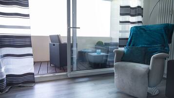 Ein modernes Zimmer mit einer Schiebetür zu einem Außenbereich, ein grauer Sessel und ein runder Tisch mit einem blauen Kissen.