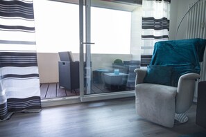 Ein modernes Zimmer mit einer Schiebetür zu einem Außenbereich, ein grauer Sessel und ein runder Tisch mit einem blauen Kissen.
