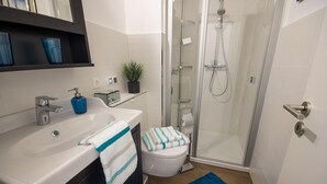 Ein modernes Badezimmer mit Dusche, Toilette, Waschbecken und einer blauen Badmatte.