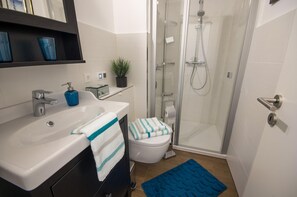 Un baño moderno con ducha, inodoro, lavamanos y una alfombra de baño azul.