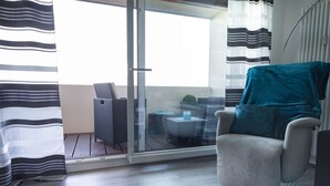 Una habitación moderna con puerta corrediza de vidrio que da a un espacio exterior, un sillón gris y una mesita redonda con un cojín azul.