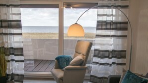 Una habitación con vista a la playa, una silla, una lámpara de pie y cortinas a rayas.
