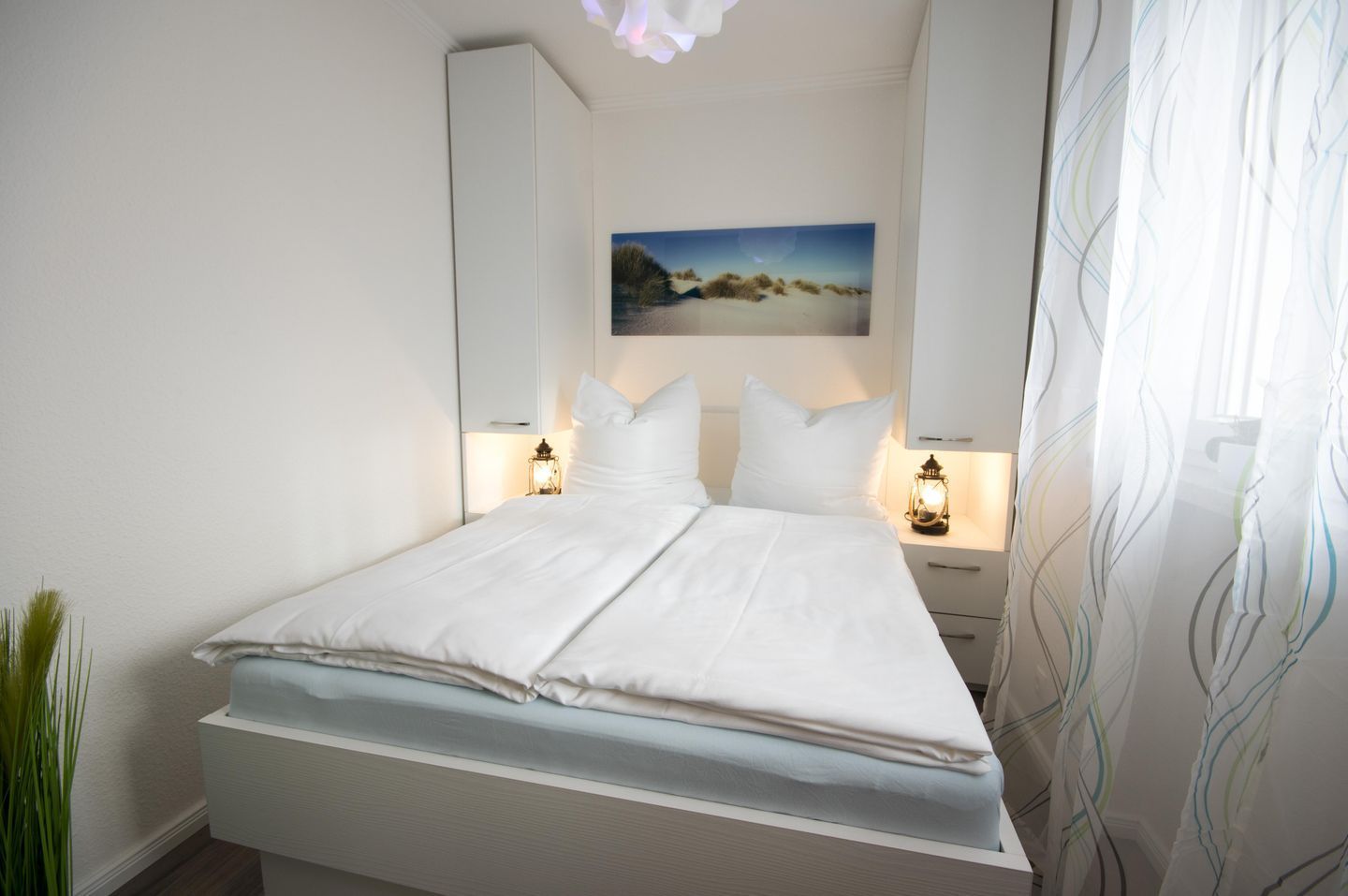 Ein ordentlich bezogenes Bett mit weißen Leinen, ein Gemälde darüber und zwei Nachttischlampen.
