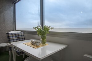 Une petite table ornée d’un vase de fleurs et d’un petit objet décoratif, avec une vue sur la mer par la fenêtre.