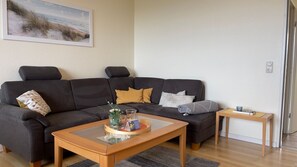 Ein Wohnzimmer mit einem dunkelbraunen Sofa, einem Glastisch und einem kleinen Holztisch.