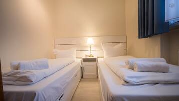 Quarto de hotel com duas camas de solteiro, mesa de cabeceira com abajur e televisão na parede.